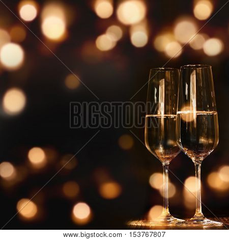 Two Champagne glasses for festive occasions in front of a dark background with golden lights and bokeh