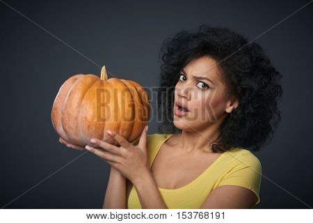 Sullen woman holding ripe pumpkin isolated over grey background
