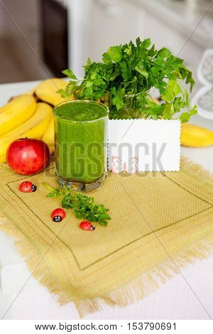 A glass of delicious healthy natural green smoothie with fresh lettuce, mint, dill, parsley and banana on the kitchen table on a napkin canvas. Healthy food, breakfast vegetarian raw food.