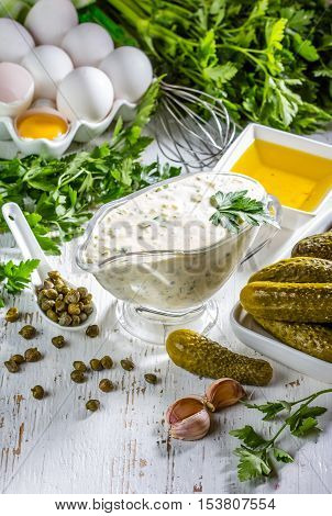 Homemade sauce tartar tartara with ingredients eggs olive oil lemon, capers, parsley, pickles on white background
