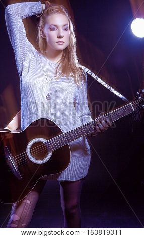Portrait of Caucasian Expressive Blond Female Posing with Guitar Against Black. Combination of Flash and Halogen Used. Vertical Image Composition