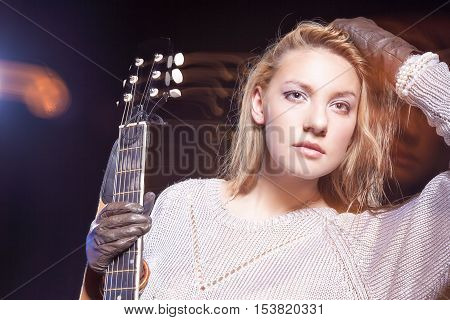 Music Concept and Ideas. Young Blond Female Posing with Guitar Against Black. Combination of Flash and Halogen Used. Horizontal Image Orientation
