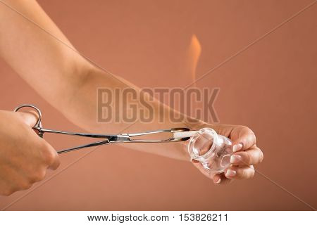 Close-up Of A Therapist Holding Lit Camphor With Tong And Cup In Spa