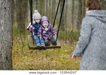 Two sisters swinging outdoors on early spring or late autumn