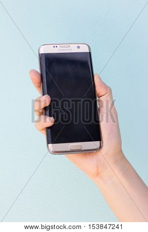 Bangkok Thailand September 10 2016 : Woman held android phone Samsung galaxy S7 Edge on blue concrete background. Samsung S7 Edge is smart phone with multi touch screen