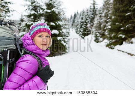 Woman hiking in white winter forest woods with backpack. Young girl walking on snowy trail. Recreation fitness and healthy lifestyle camping outdoors. Motivation and inspirational winter landscape.