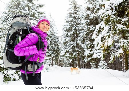 Woman hiking trekking in winter woods with akita dog. Recreation fitness and healthy lifestyle outdoors in beautiful snowy nature. Motivation and inspirational white winter landscape.