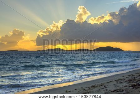 Vivid rays from rising sun shine brilliantly from behind clouds over tropical Caribbean island of Culebrita and reflect on sea and Zoni Beach on Isla Culebra