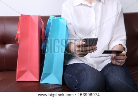Woman sit on sofa with shopping bag use smarth phone with paying money by use credit card