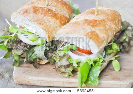 baguette sandwich with ham tomato and lettuce on wooden plate