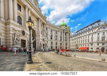 VIENNA AUSTRIA - JUNE 25 2016: Hofburg Palace seen from Michaelerplatz on sunny day with tourists and people. Vienna. Austria.