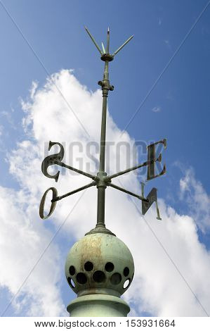 Old cardinal points (cardinal directions north east south west) on a roof with a lightning rod on blue sky with clouds
