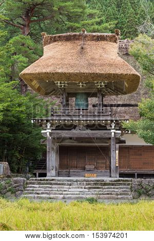 Shirakawago Japan - September 23 2016: Even the bell tower of the Myozenji Buddhist temple in Shirakawago had the particular joined-hands roof. Green foliage and yellow rice paddy.