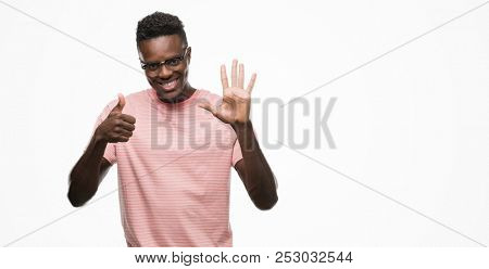 Young african american man wearing pink t-shirt showing and pointing up with fingers number six while smiling confident and happy.