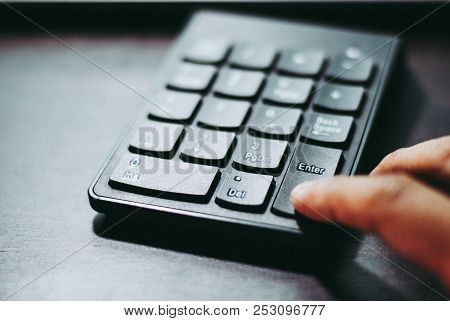 An Index Finger Is Pressing On Enter Button Of A Black Plastic Numeral Keypad In Order To Make Decis