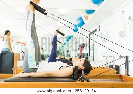 Side View Of Female Client Maintaining Her Fitness While Exercising On Reformer Machine In Gym