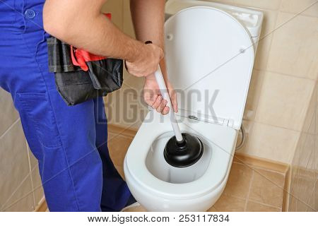 Plumber Repairing Toilet With Hand Plunger Indoors