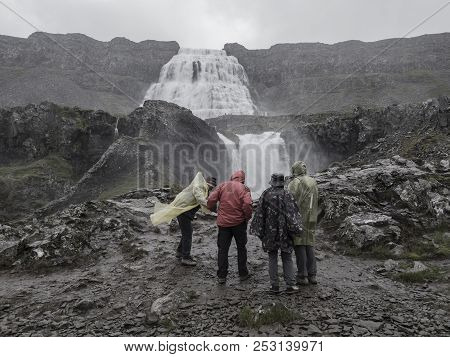 Group Of Tourist People In Colorful Raincoat Watching Dynjandi Waterfall, Biggest In West Fjords Of 