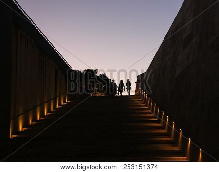 Silhouette Of Three Young Men On Big Ladder On Background Of Sunset Sky In Valletta, Malta
