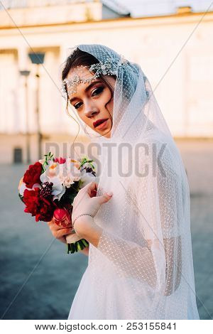 Beautiful Eastern Style Bride With White Veil And Hairpiece Holding Bridal Bouquet Posing Outdoors A
