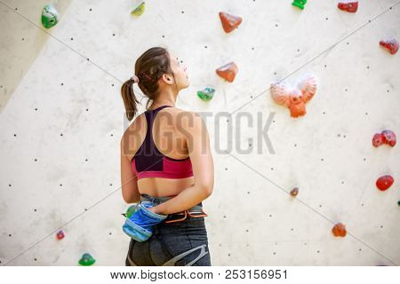 Photo from back of woman athlete with bag of talc against background of wall for rock climbing