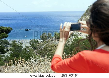 Greek Island, Young Woman Taking A Panorama Photo Of The Beach With Mobile Phone