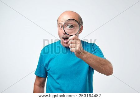 Elderly Man In Blue T-shirt Looking Through A Magnifying Glass. Concept Of Quality Control Checking.