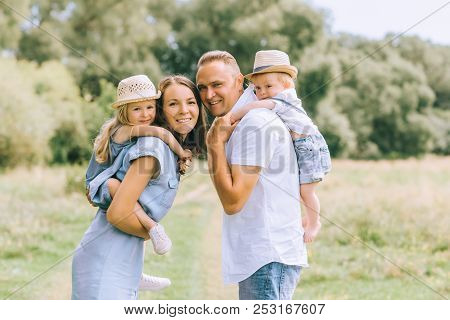 Parents Piggybacking Children In Straw Hats On Summer Feild