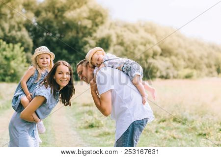 Happy Parents Piggybacking Son And Daughter In Straw Hats On Summer Feild