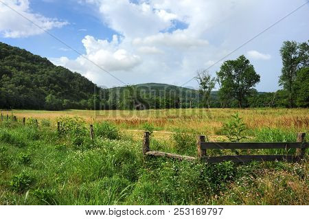 Landscape Image Of Old, Wooden Barn Nestled In A Field With Trees.  Ozark Mountains Rise Around Rust