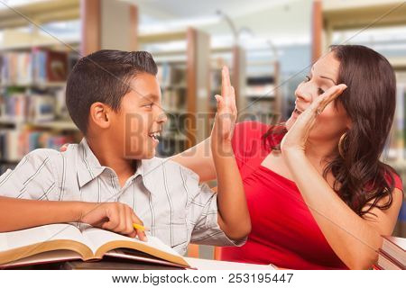 Hispanic Young Boy and Famle Adult High Five Whilte Studying At Library.
