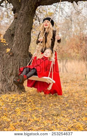 Beautiful Mother In A Long Dress Is Swinging On A Hinged Swing Little Daughter In A Red Coat In An A
