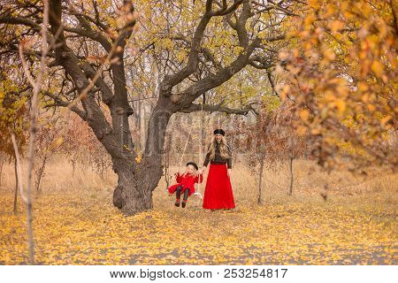 Beautiful Mother In A Long Dress Is Swinging On A Hinged Swing Little Daughter In A Red Coat In An A