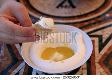 A Man Dipping A Pita Bread Slice In Labneh And Offering It.