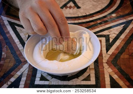 A Man Dipping A Pita Bread Slice In Labneh And Olive Oil.