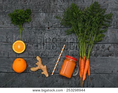 Freshly Made Carrot Smoothie, Bunch Of Carrots, Orange And Ginger Root On A Rustic Dark Table. The V