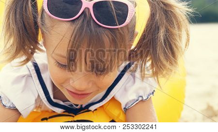 Portrait Of A Cute Smling Girl Wearing Sunglasses On The Forehead, , Sitting On Summer Beach.
