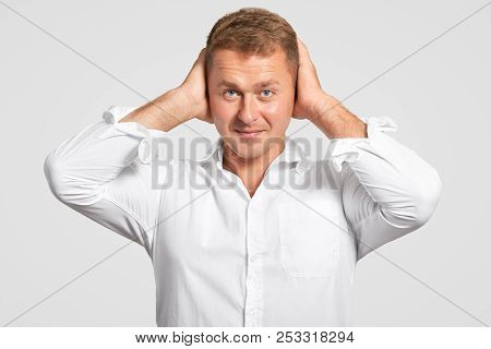 Studio Shot Of Successful Young Male Entrepreneur Keeps Hands On Head, Looks Seriously At Camera, Dr
