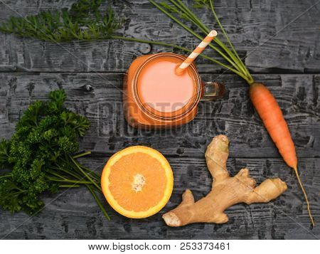 Freshly Made Carrot Smoothie, Carrot, Parsley, Orange And Ginger Root On A Rustic Table. The View Fr