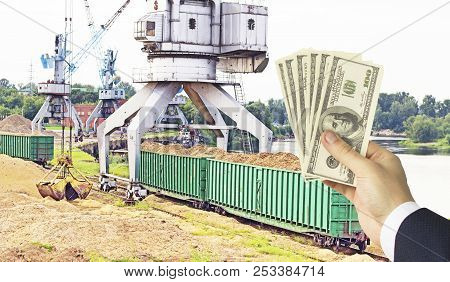 Hand With Money Dollars On The Background Of A Port Crane Produces The Loading Of Wood Chips Into Fr