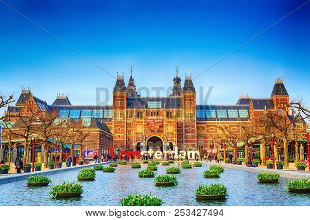 Amsterdam, Netherlands - March 31, 2016: Water And Flowers, Rijksmuseum And People In Front Of Writi