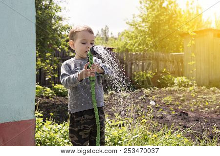 A Child In The Garden Watering Flowers, A Little Boy With A Water Hose Watering The Garden