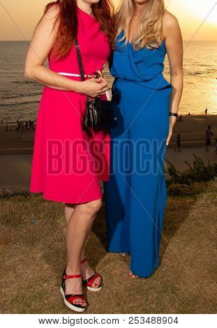 Two Girls Are Alone In A Red Dress, The Other In A Blue Trouser Suit Full-length With No Heads On Th