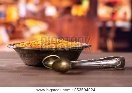 Lot Of Whole Raw Red Lentils And Sugar Tongs In Old Iron Bowl With Rustic Wood Kitchen In Background