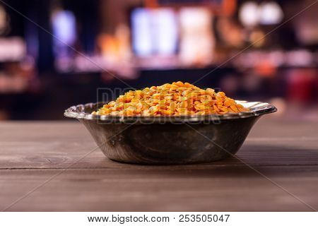 Lot Of Whole Raw Red Lentils In Old Iron Bowl With Restaurant In Background