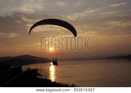 Silhouette Of Paramotor Flight Over River With Sunset