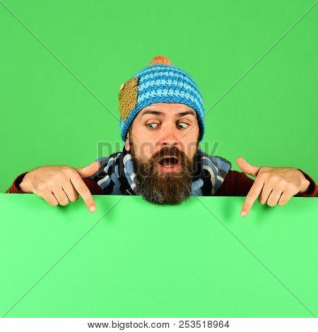 Man In Warm Hat Points Down On Green Background