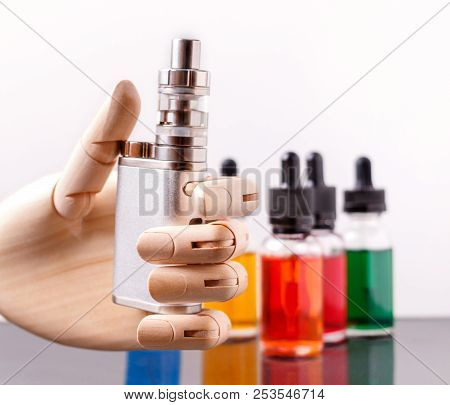 Mannequin Hand Holding Electronic Cigarette. Bottles With Vape Liquid On Background