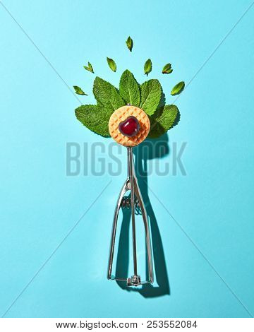 Creative composition from mint leaves in the metal spoon for ice cream and biscuit with cherry on a blue glass background with shadows. Food modern style, top view.
