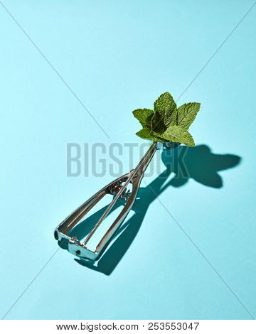 Creative composition from mint leaves in the metal spoon for ice cream on a blue glass background with shadows. Food modern style.